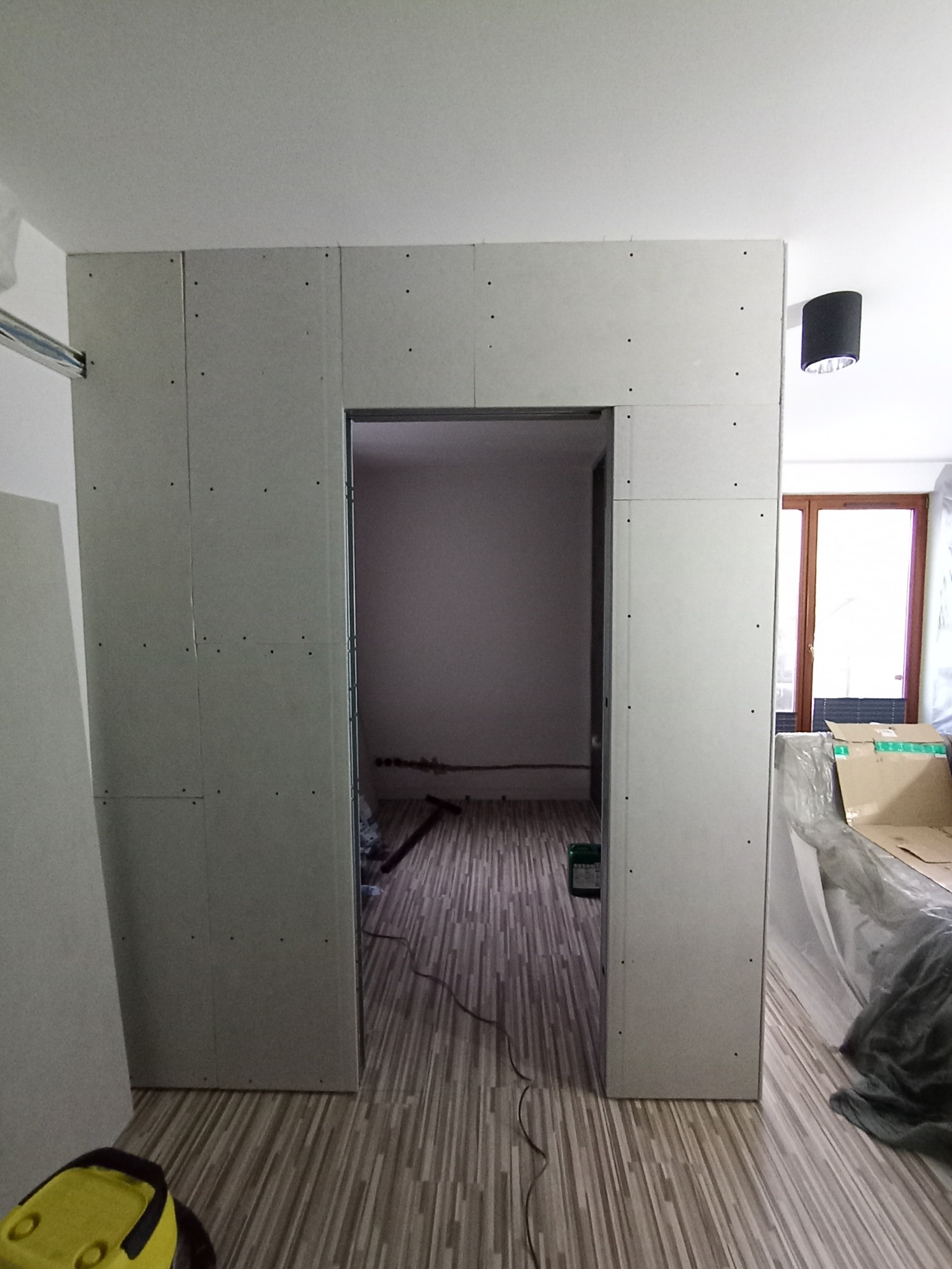 Ściana działowa z płyt gipsowo-kartonowych z wyciętym otworem na drzwi, widok na wnętrze pomieszczenia z parkietem. Etap prac wykończeniowych.