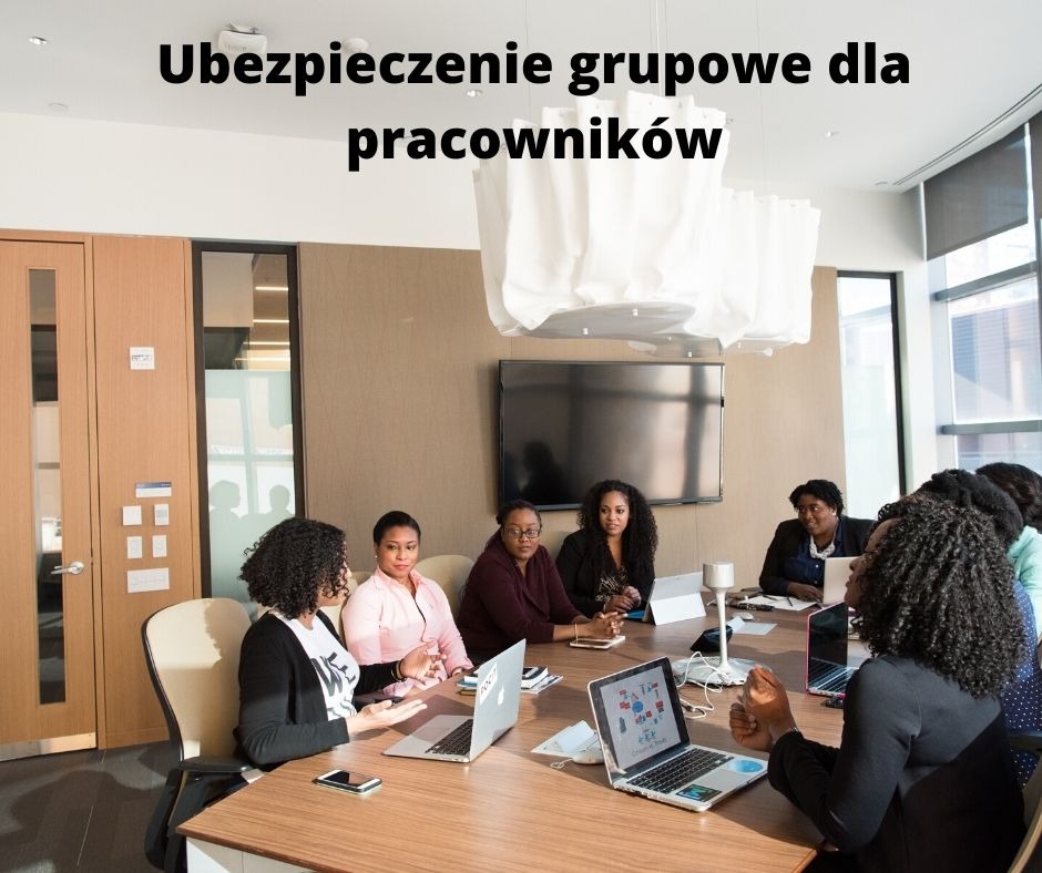 Grupa pracowników w sali konferencyjnej podczas spotkania, na stole laptopy i telefony komórkowe, w tle okno z widokiem na miasto.