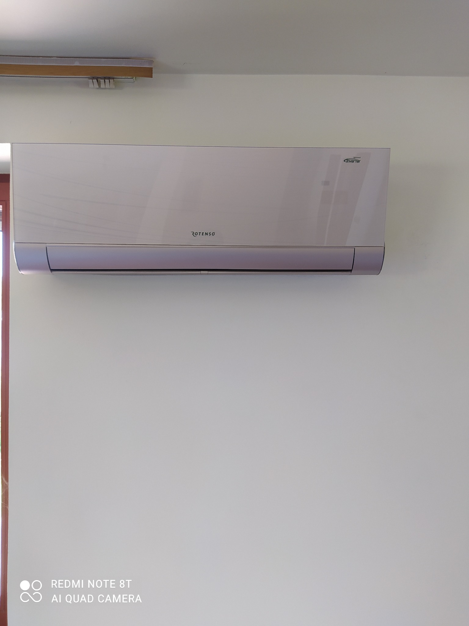 Biały klimatyzator Rotenso Inverter zamontowany na białej ścianie, widoczne oznaczenie Inverter na obudowie.