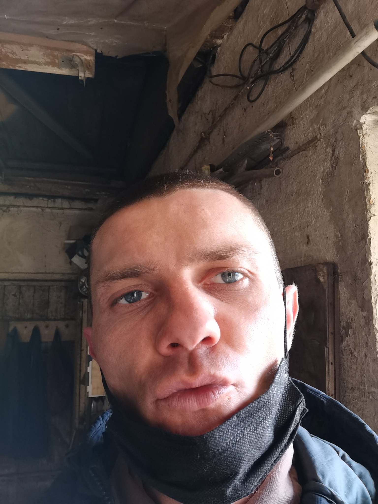 Mężczyzna w masce na tle surowego wnętrza w trakcie remontu, widoczne przewody i stara ściana.