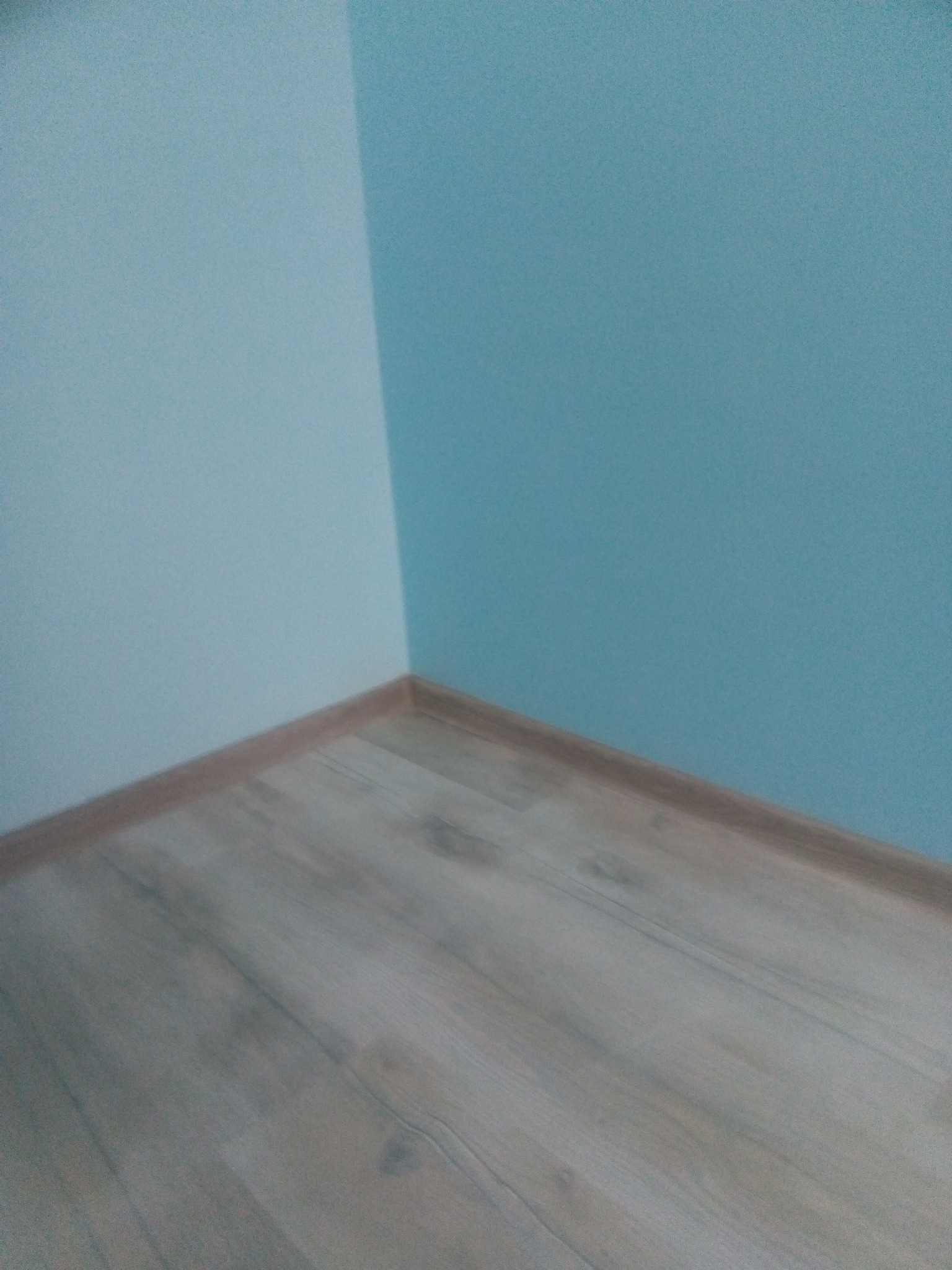 Róg pokoju po odświeżeniu: ściany pomalowane na dwa odcienie błękitu, jasna podłoga z paneli z brązowymi listwami przypodłogowymi.