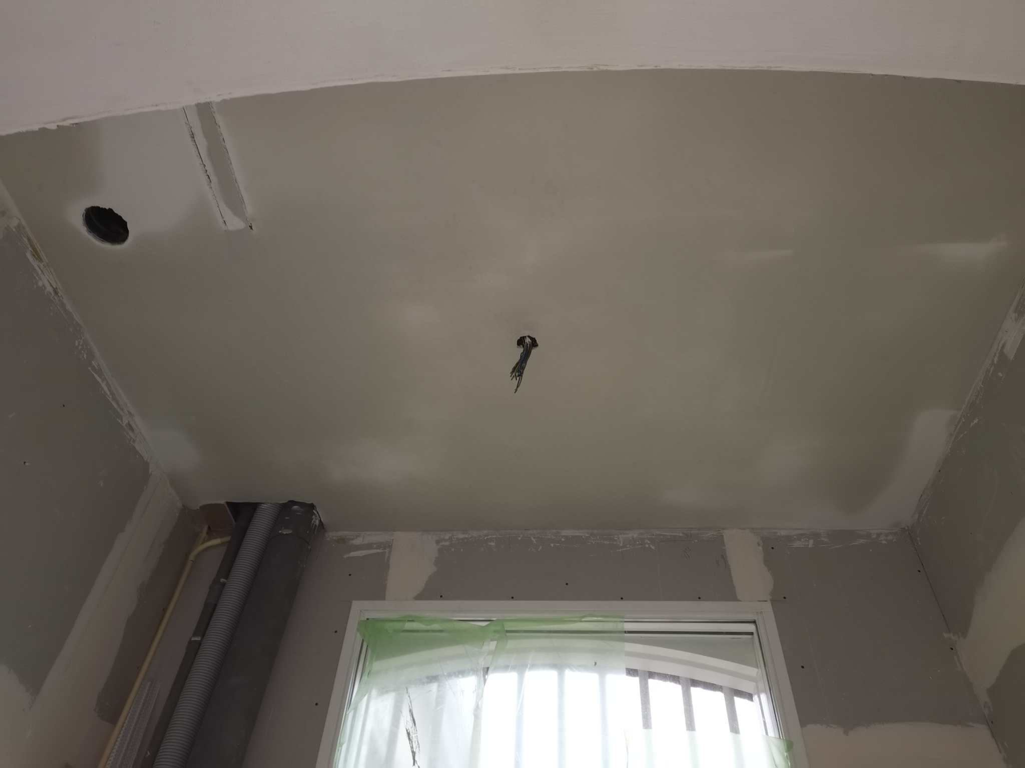 Sufit z płyt kartonowo-gipsowych, częściowo wykończony, widoczne łączenia płyt, otwór na oświetlenie oraz przewody elektryczne, okno zabezpieczone folią malarską.