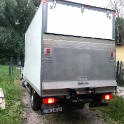 Tył białego busa dostawczego marki Trouillet Dhollandia z otwartymi drzwiami, widoczne światła i tablica rejestracyjna CTR 24769, zaparkowanego na szutrowej drodze w otoczeniu zieleni.
