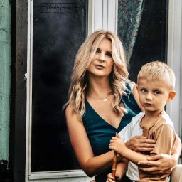 FotoArt Monika Górniak - Portret mamy z synkiem w Kołobrzegu na tle okna. Kobieta w zielonej sukience, chłopiec trzyma bambusowy kijek. Naturalne światło, spokojna atmosfera.