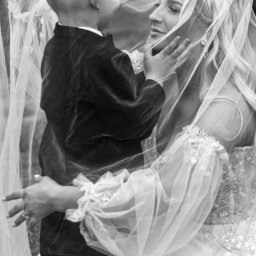 FotoArt Monika Górniak - Czarno-białe ujęcie panny młodej w welonie, delikatnie dotykanej przez małego chłopca w eleganckim ubraniu. Romantyczna atmosfera, subtelne światło.