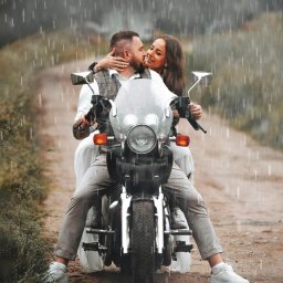 FotoArt Monika Górniak - Uśmiechnięta para na motocyklu w deszczu, kobieta obejmuje mężczyznę. Romantyczna sesja w plenerze, brązowe tło, stylowe ubrania i białe buty.