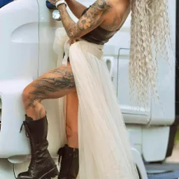 Kobieta z tatuażami w stylizowanej sukni i butach na tle kabiny ciężarówki. Nietypowa sesja fotograficzna z mocnym kontrastem stylów i elementem motoryzacyjnym.