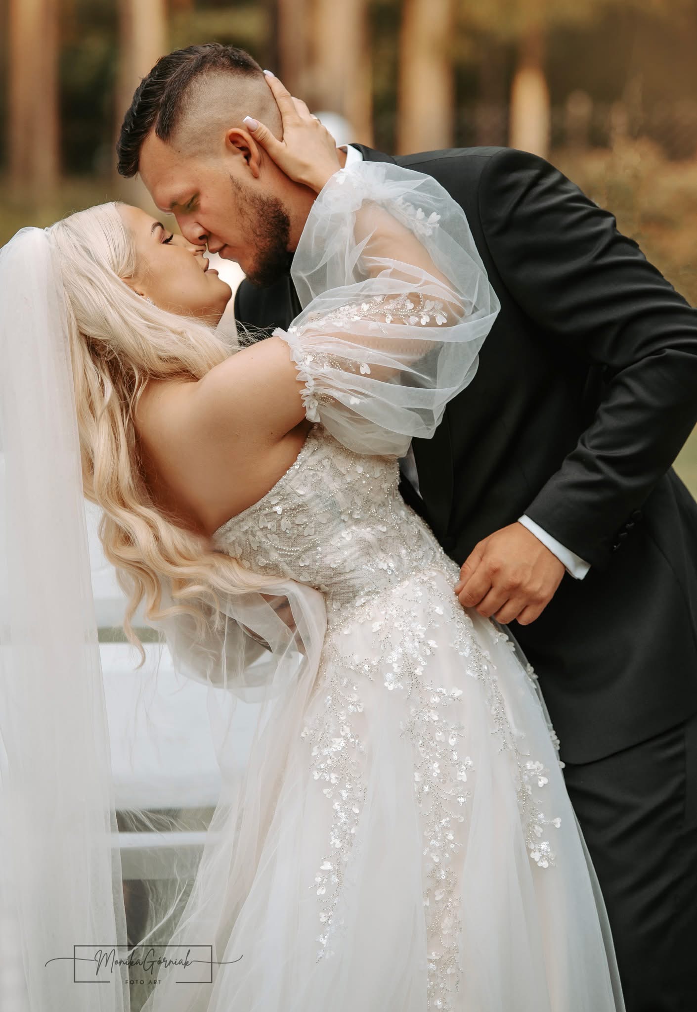 Para młoda w objęciach podczas pocałunku. Panna młoda w sukni z delikatnymi zdobieniami, pan młody w czarnym garniturze. Romantyczna atmosfera ślubna.