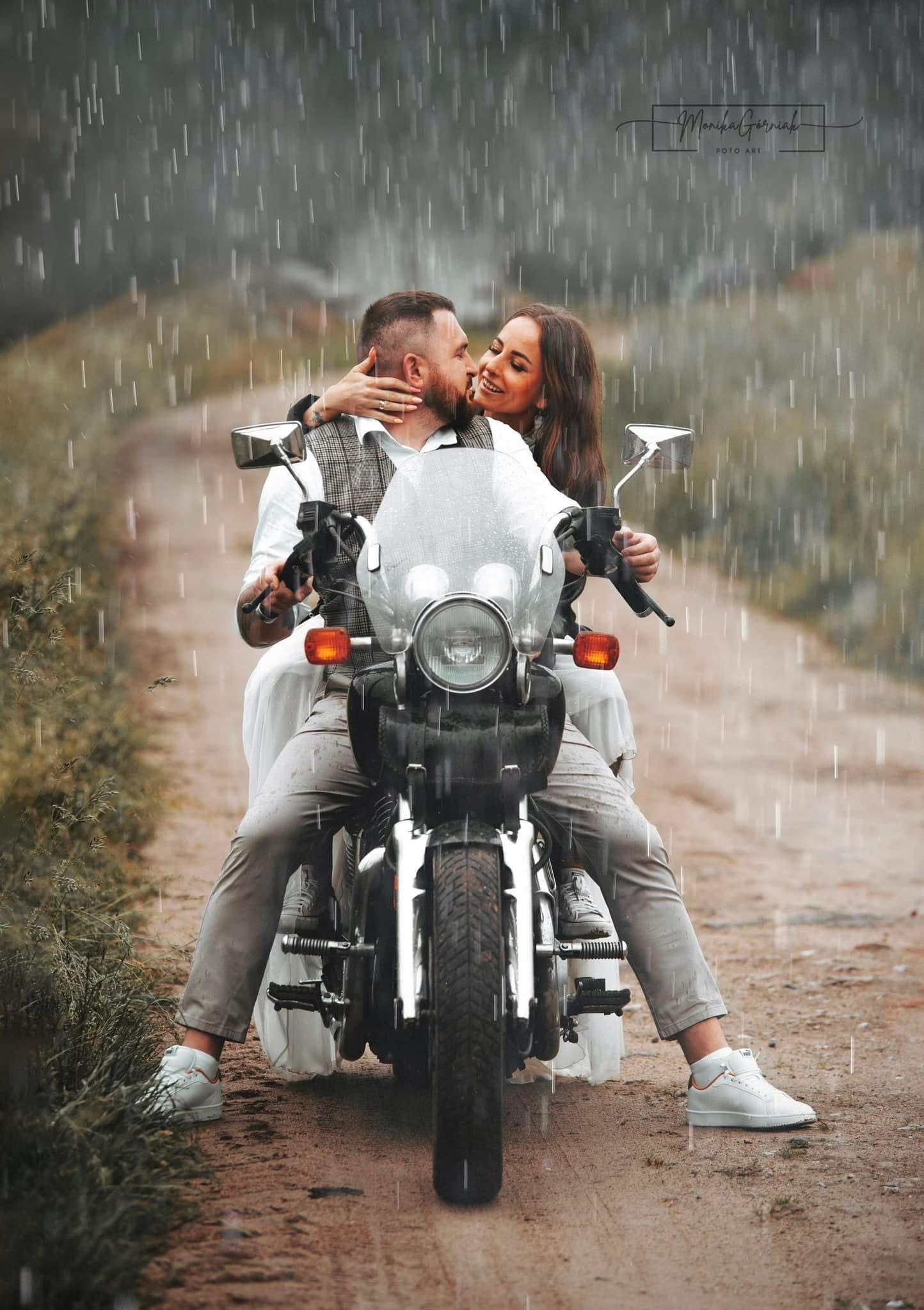 Uśmiechnięta para na motocyklu w deszczu, kobieta obejmuje mężczyznę. Romantyczna sesja w plenerze, brązowe tło, stylowe ubrania i białe buty.