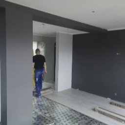 Walldonegk - Wnętrze w trakcie wykończenia: szare ściany, częściowo położona podłoga, pracownik w oddali.