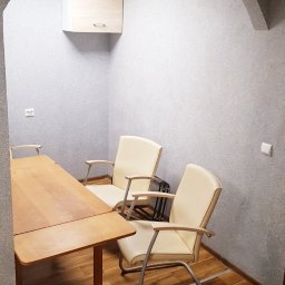 Standart Traweling sp.z o.o - Biuro z drewnianym stołem i krzesłami z kremową tapicerką, wykończone ścianami o szarej, ziarnistej fakturze i łukowatym przejściem.