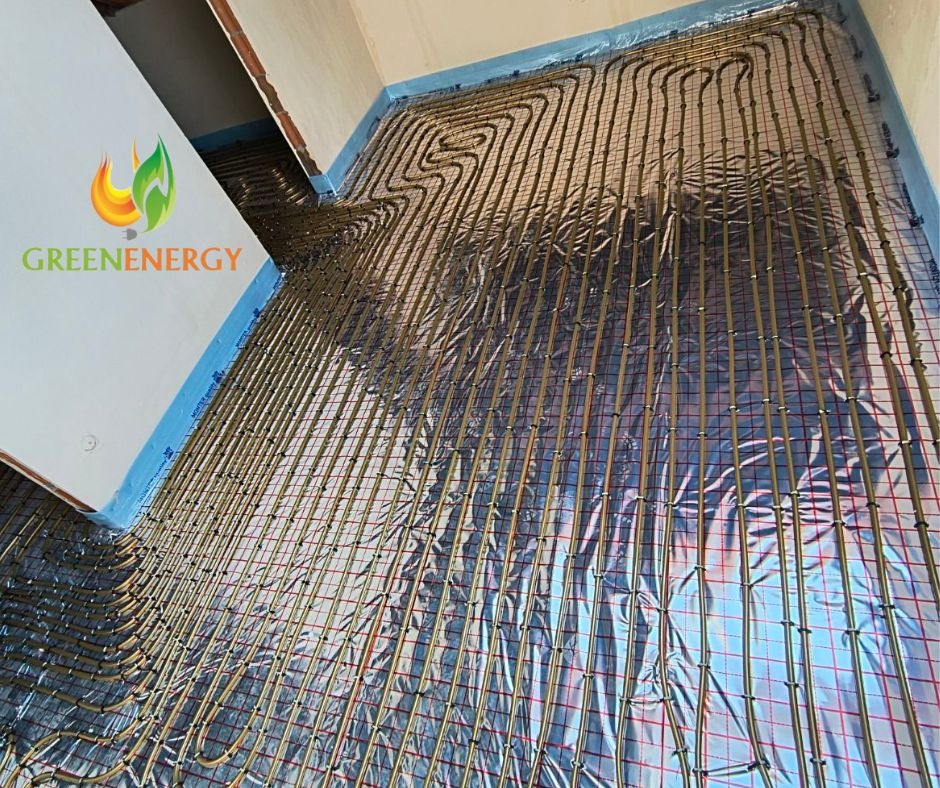 Instalacja ogrzewania podłogowego z rurkami układanymi w pętle na folii termoizolacyjnej i siatce montażowej, widoczne logo firmy Green Energy na ścianie.