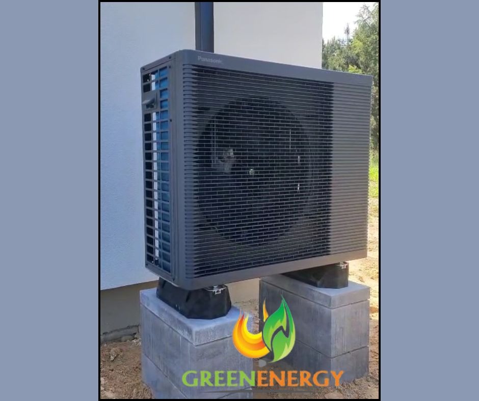 Zamontowana, zewnętrzna jednostka pompy ciepła Panasonic na betonowych bloczkach, z logo GreenEnergy w rogu. Widok z boku na tle ściany budynku.