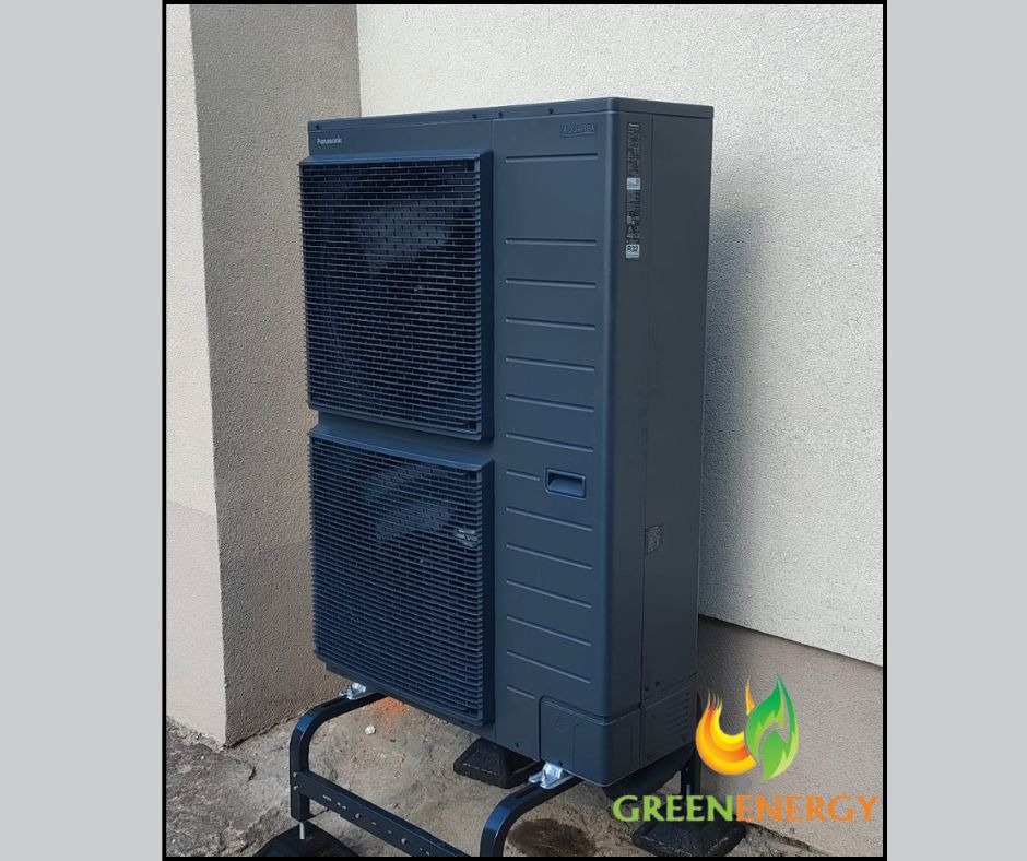 Zewnętrzna jednostka pompy ciepła Panasonic Aquarea na czarnym stelażu, ustawiona przy ścianie budynku. Widoczne logo GreenEnergy w prawym dolnym rogu.