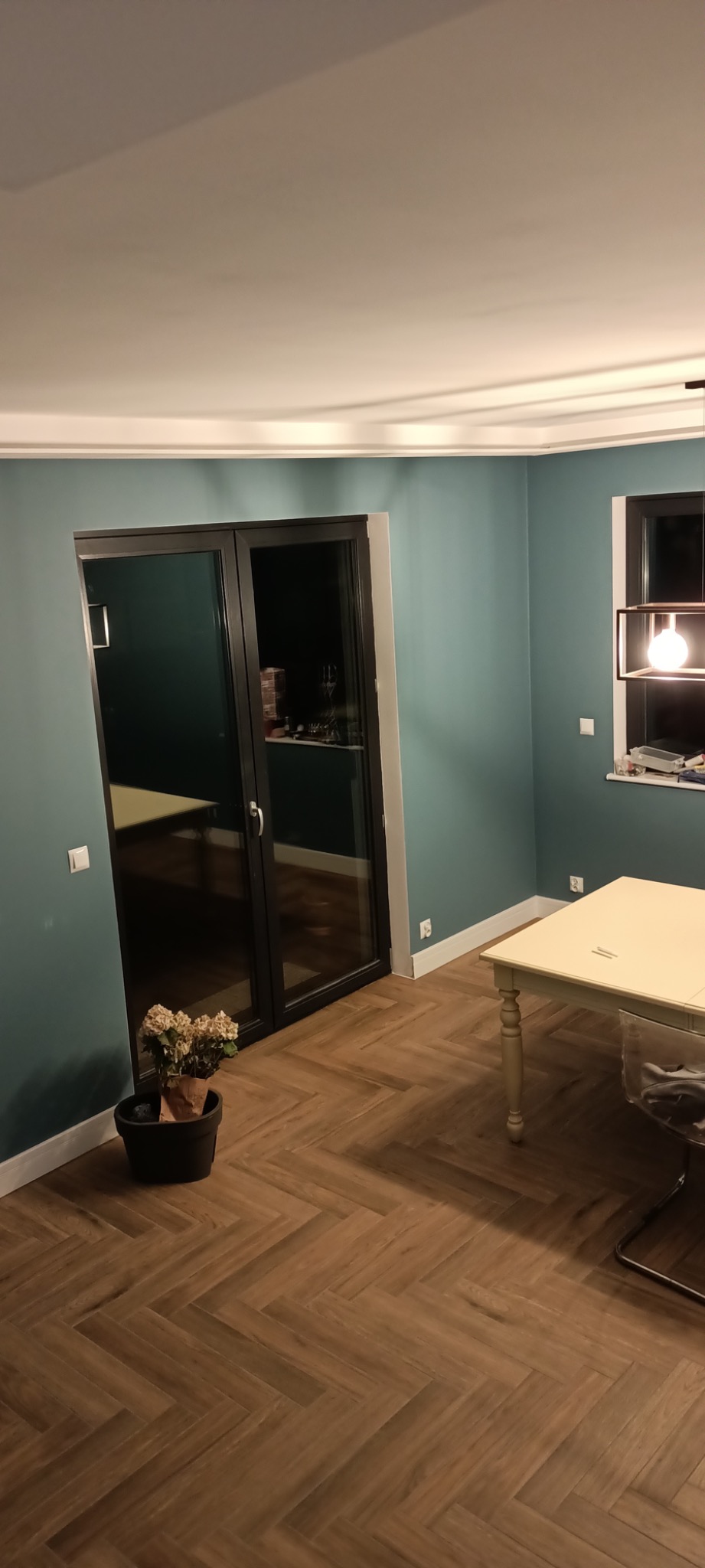 Pokój po remoncie z parkietem ułożonym w jodełkę, turkusowe ściany, czarne drzwi przesuwne i kremowy stół z krzesłem