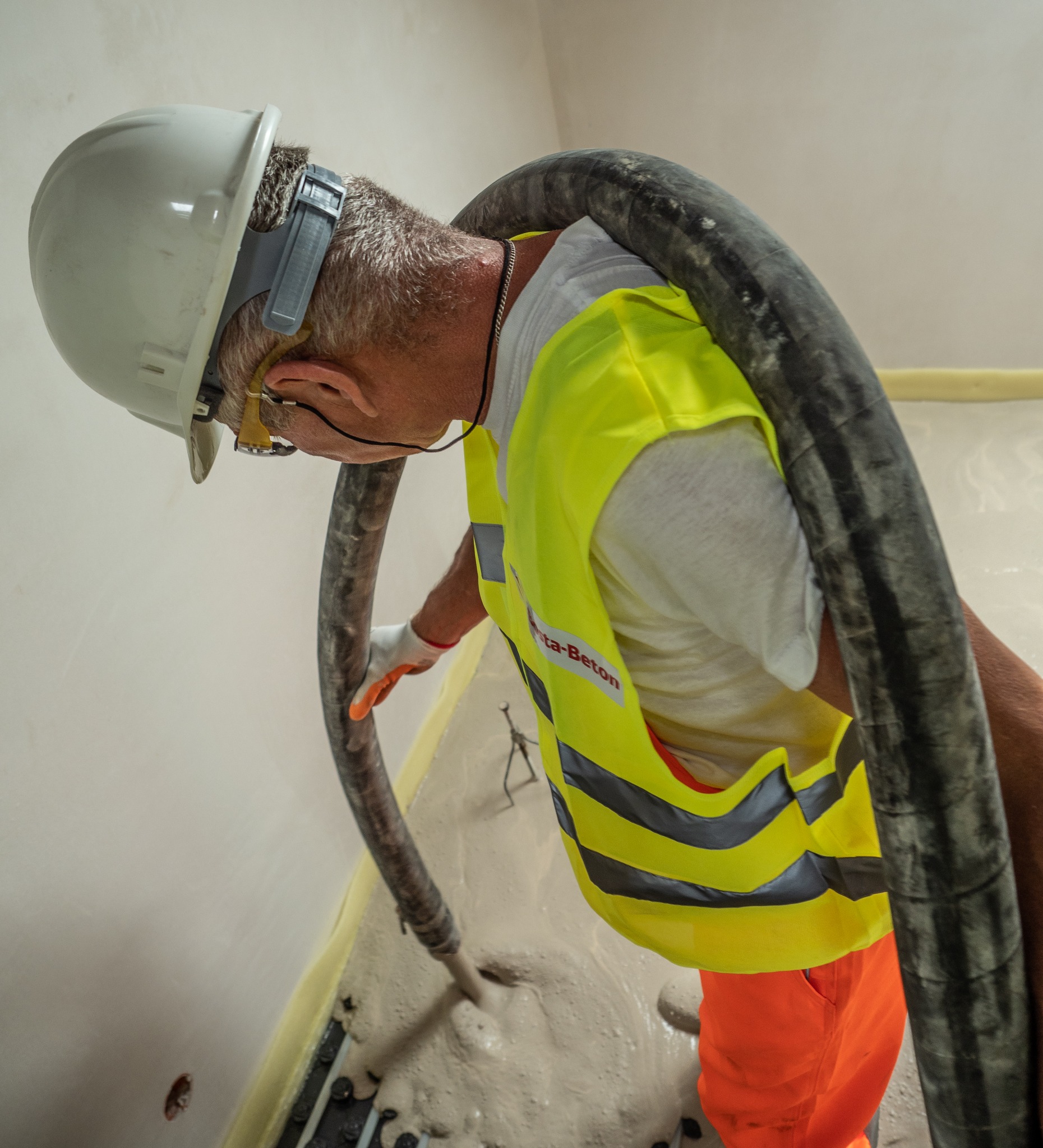 Pracownik w kasku i kamizelce Beta-Beton w trakcie wylewania anhydrytu na ogrzewanie podłogowe za pomocą pompy.