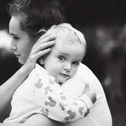 Anna Kula Fotografia - Czarno-białe zdjęcie matki obejmującej małe dziecko w ubraniu z motywem Myszki Miki, dziecko patrzy w obiektyw z delikatnym uśmiechem.