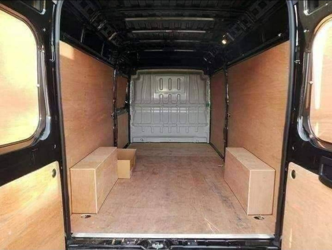 Wnętrze pustej furgonetki wyłożonej sklejką, z dwoma kartonowymi pudłami po bokach, przygotowanej do transportu lub przeprowadzki.