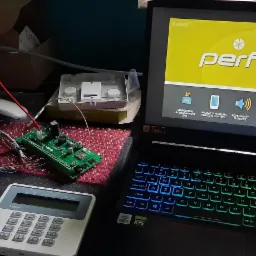 Konfiguracja systemu alarmowego Perfecta w Zagrodnie: laptop z uruchomionym oprogramowaniem, centrala alarmowa, moduł elektroniczny z przewodami, elementy obudowy na biurku.