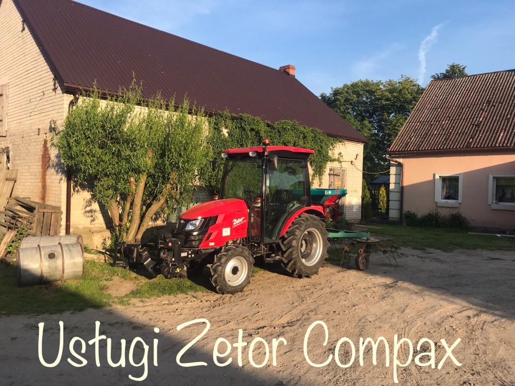 Czerwony traktor Zetor Compax z podłączonym sprzętem rolniczym stoi na piaszczystym podwórku przed budynkami gospodarczymi z brązowymi dachami.