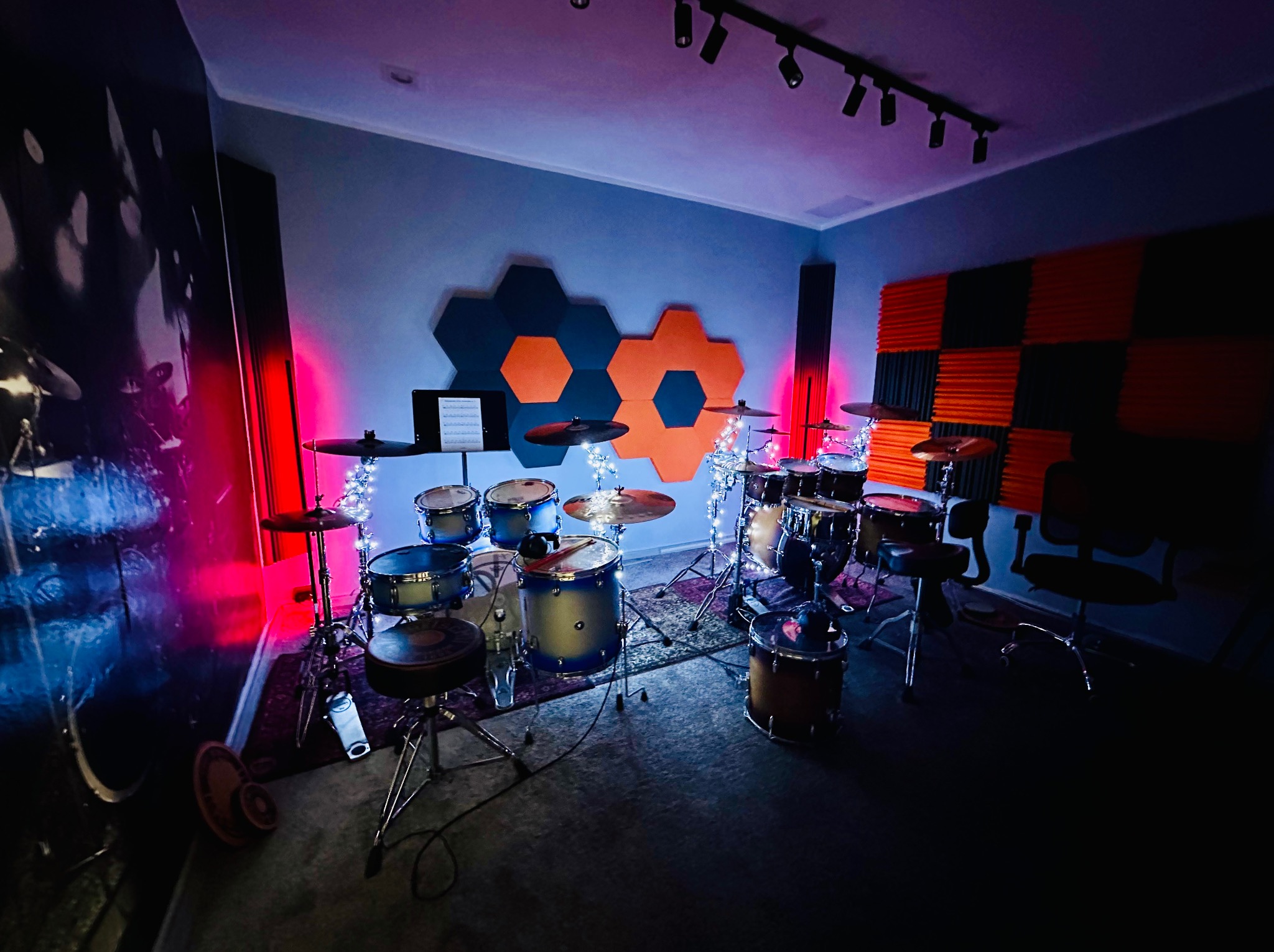 Zestaw perkusyjny w studio nagrań w Chorzowie, z elementami wygłuszającymi na ścianach, oświetlony lampkami i czerwonymi lampami. Na ścianie widoczny abstrakcyjny mural.