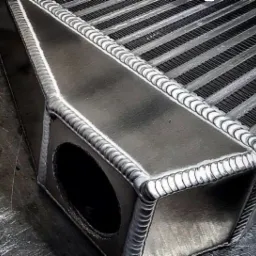 Szczegółowe ujęcie spawów na aluminiowym intercoolerze, ukazujące precyzję i jakość wykonania, z widoczną strukturą żeber chłodzących.
