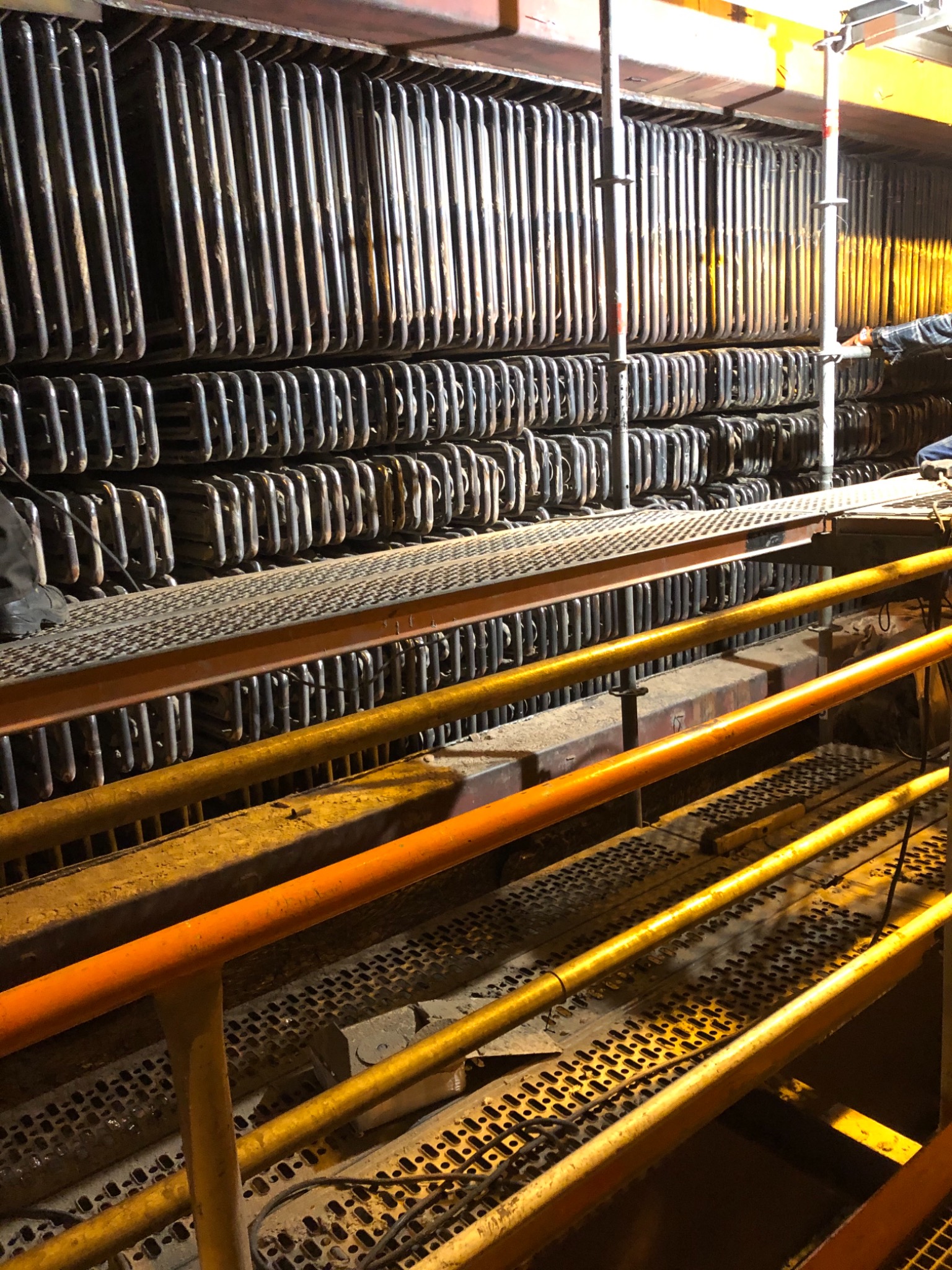 Wnętrze przemysłowego kotła z rzędami rur, widoczne pomosty robocze i fragment sylwetki pracownika.