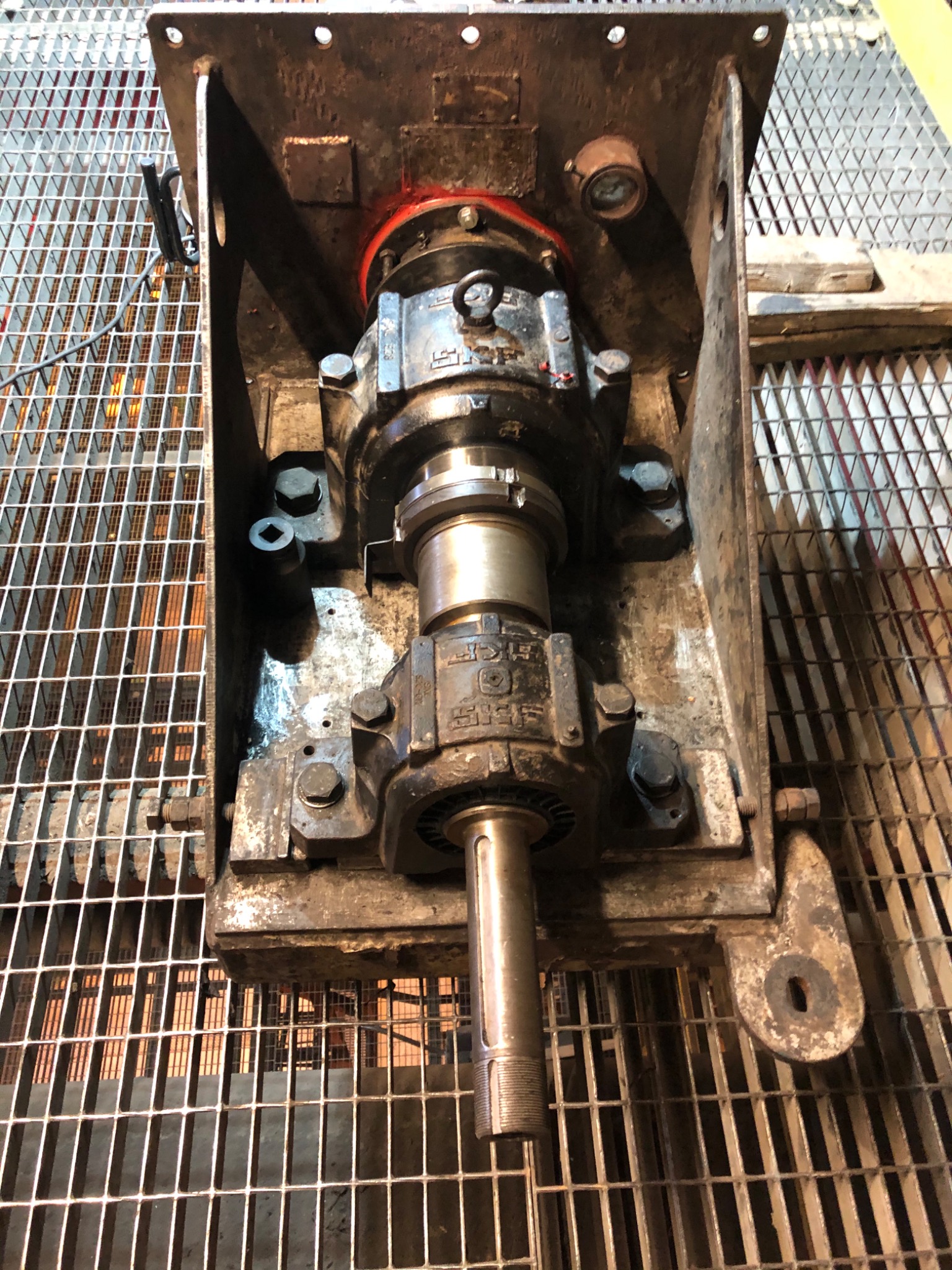 Widok z góry na zamontowany, metalowy mechanizm łożyskowy z wystającym gwintowanym wałem, umieszczony w metalowej ramie kratownicowej, z widocznymi śladami użytkowania i smarowania.