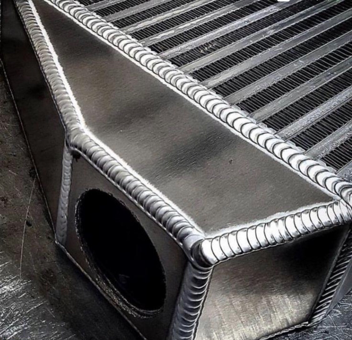 Szczegółowe ujęcie spawów na aluminiowym intercoolerze, ukazujące precyzję i jakość wykonania, z widoczną strukturą żeber chłodzących.