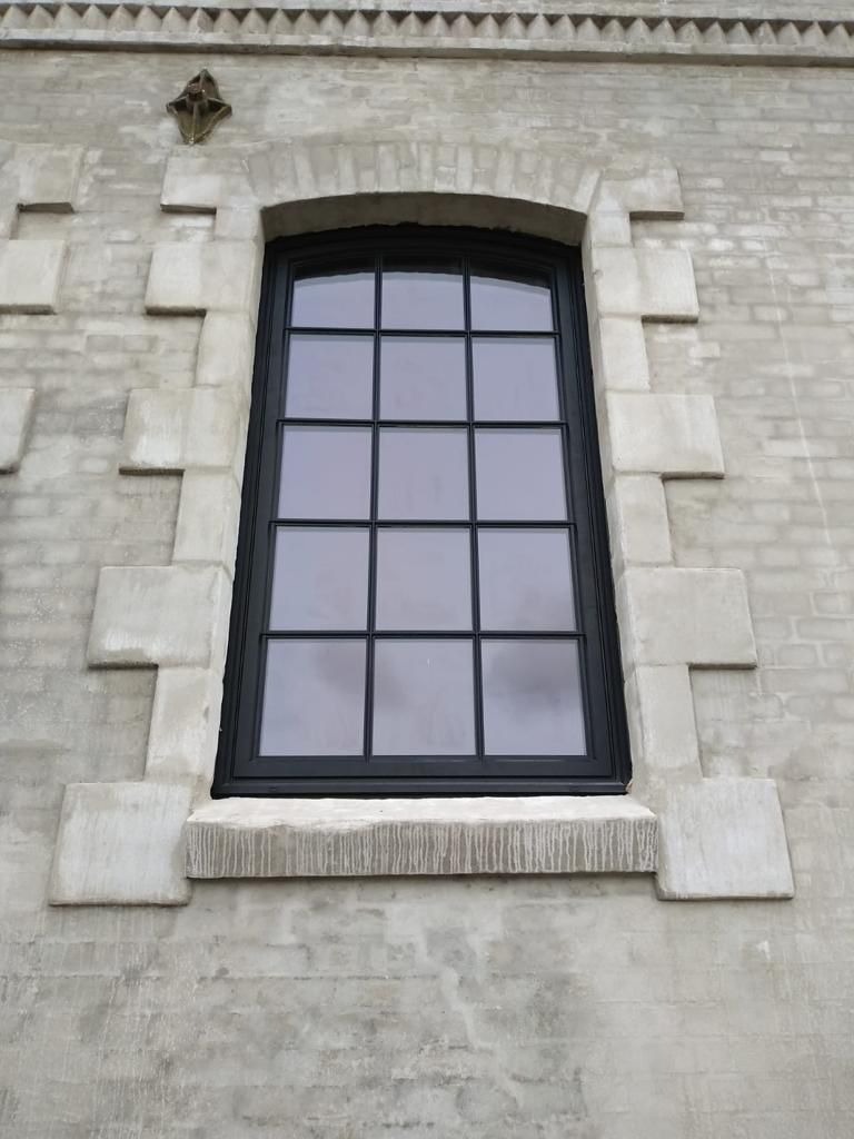 Czarne okno z podziałami na szprosy w kamiennej elewacji z dekoracyjnymi elementami.