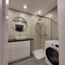 Fenix Grzegorz Woźniak - Nowoczesna łazienka w szarościach z okrągłym lustrem, białą umywalką nablatową, kabiną prysznicową ze szklanymi ściankami i pralką Whirlpool