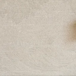 Beżowa płytka ceramiczna z subtelnym, wytłoczonym napisem 'VERSACE'.