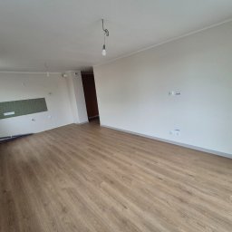 Fenix Grzegorz Woźniak - Jasne panele podłogowe w nowym wnętrzu, ściany w odcieniach bieli, widoczne instalacje hydrauliczne i elektryczne. Minimalistyczny design, surowy stan wykończenia.