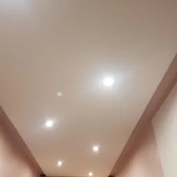 Pomieszczenie z podwieszanym sufitem z wbudowanymi punktowymi lampami LED, ściany w odcieniach różu, widoczne szafki i fragment drzwi.