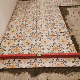 damian - Układanie wzorzystych płytek podłogowych w trakcie remontu w Warszawie, poziomica spoczywa na świeżo położonych płytkach, widoczny laser krzyżowy.