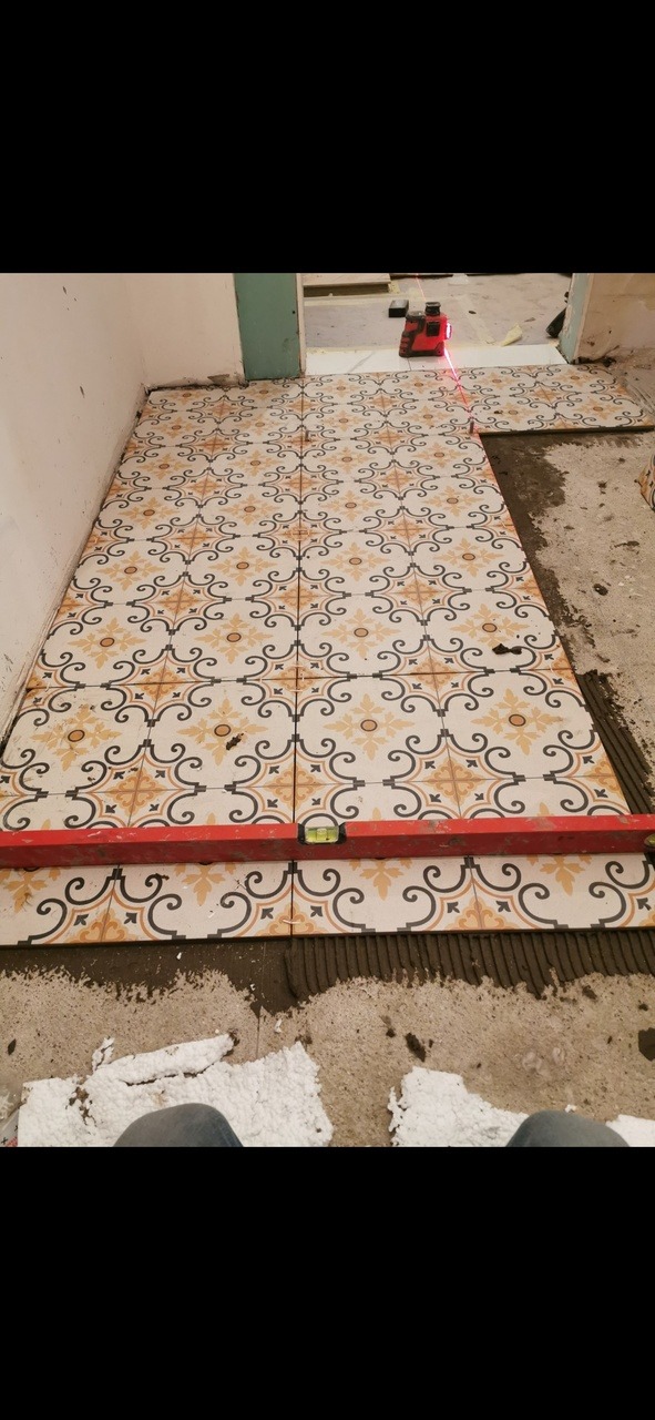 Układanie wzorzystych płytek podłogowych w trakcie remontu w Warszawie, poziomica spoczywa na świeżo położonych płytkach, widoczny laser krzyżowy.