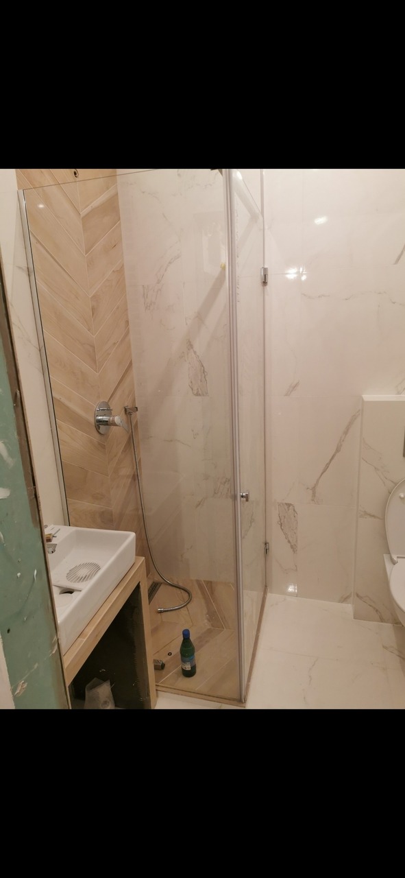 Montaż kabiny prysznicowej z elementami wykończenia w jodełkę, widoczne narzędzia i butelka po napoju.