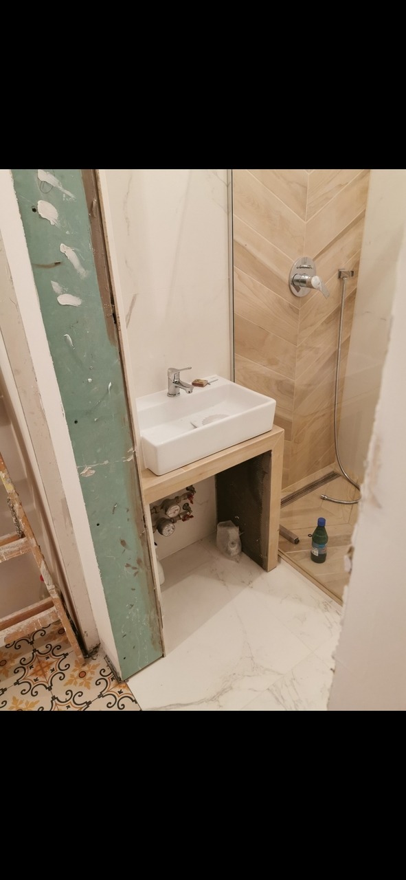 Montaż umywalki nablatowej w łazience z ułożonymi płytkami imitującymi drewno w strefie prysznica, widoczne elementy instalacji wodnej i niedokończone prace wykończeniowe.