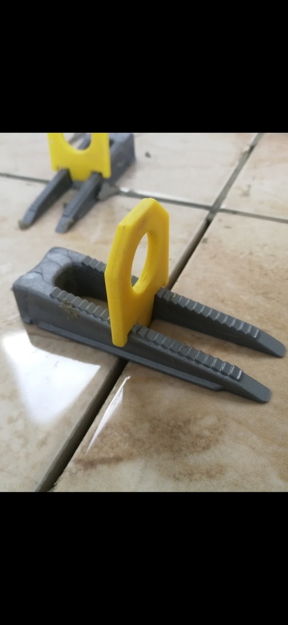 System poziomowania płytek: szare klipsy i żółte kliny na kremowych płytkach podłogowych, widoczne szczeliny między płytkami.