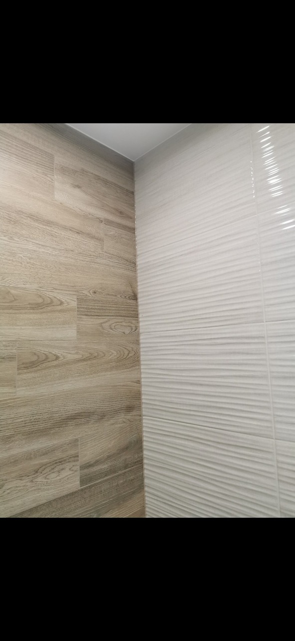 Białe, faliste płytki ceramiczne na ścianie zestawione z drewnopodobnymi płytkami na podłodze i ścianie, tworzące kontrastującą, nowoczesną aranżację narożnika łazienki.