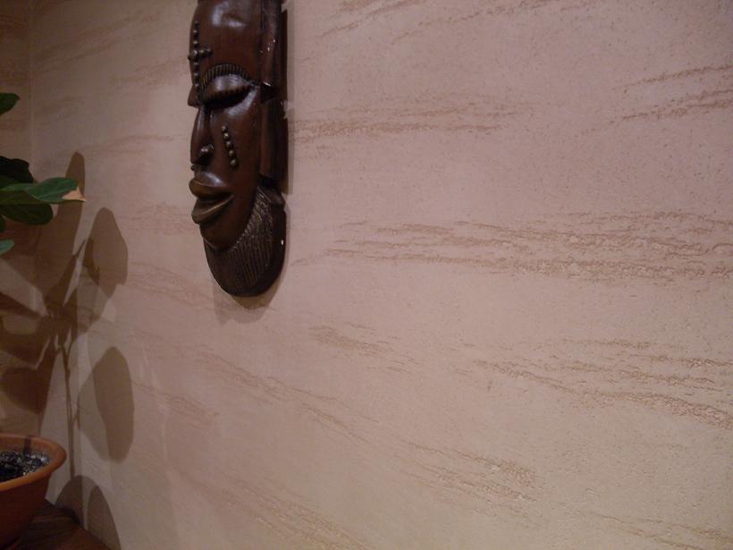 Teksturowana ściana w odcieniach beżu z dekoracyjną, drewnianą maską afrykańską, oświetlona ciepłym światłem