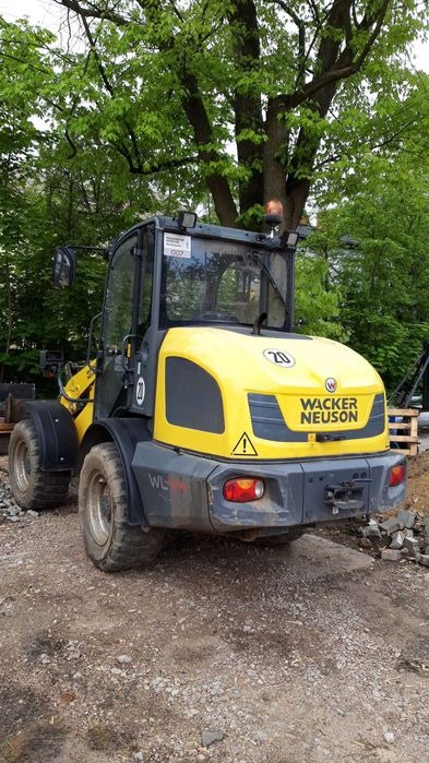 Żółto-szara ładowarka Wacker Neuson na żwirowym podłożu, z zielonymi drzewami w tle.