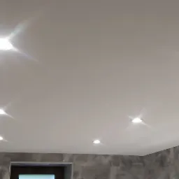 Biały sufit napinany z sześcioma punktowymi lampami halogenowymi, szare płytki na ścianie, fragment szafki i podwójny kinkiet w łazience.