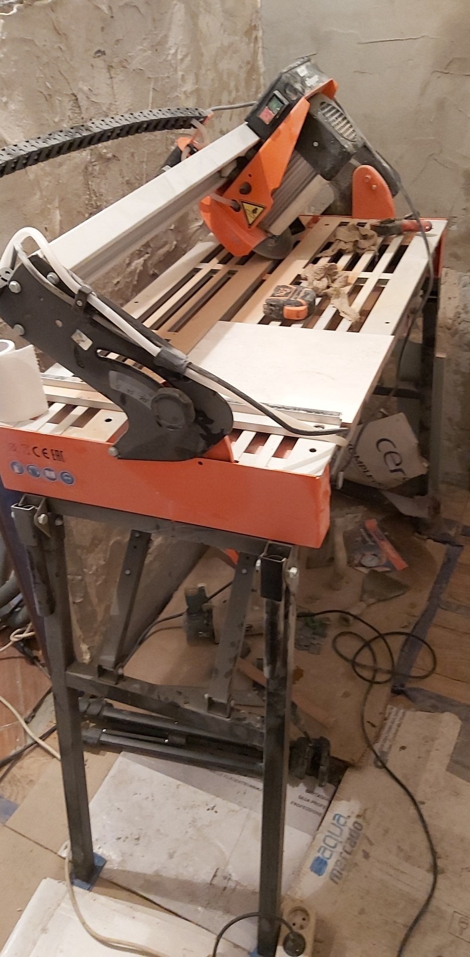 Elektryczna przecinarka do płytek z tarczą diamentową, przygotowana do cięcia jasnej płytki na tle surowej ściany i podłogi w trakcie prac remontowych.