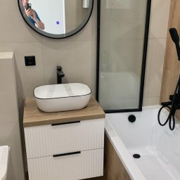 ELŻBIETA MIELNICKA ELIX - Nowoczesna łazienka z owalną umywalką nablatową z czarnym rantem, baterią w kolorze czarnym, okrągłym lustrem z podświetleniem, kabiną prysznicową z czarnymi profilami i wanną obudowaną płytkami...