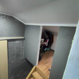 ELŻBIETA MIELNICKA ELIX - Szare ściany w trakcie malowania w pomieszczeniu na poddaszu, widoczne schody, fragment szafy przesuwnej i wejście do garderoby z maszyną do szycia.