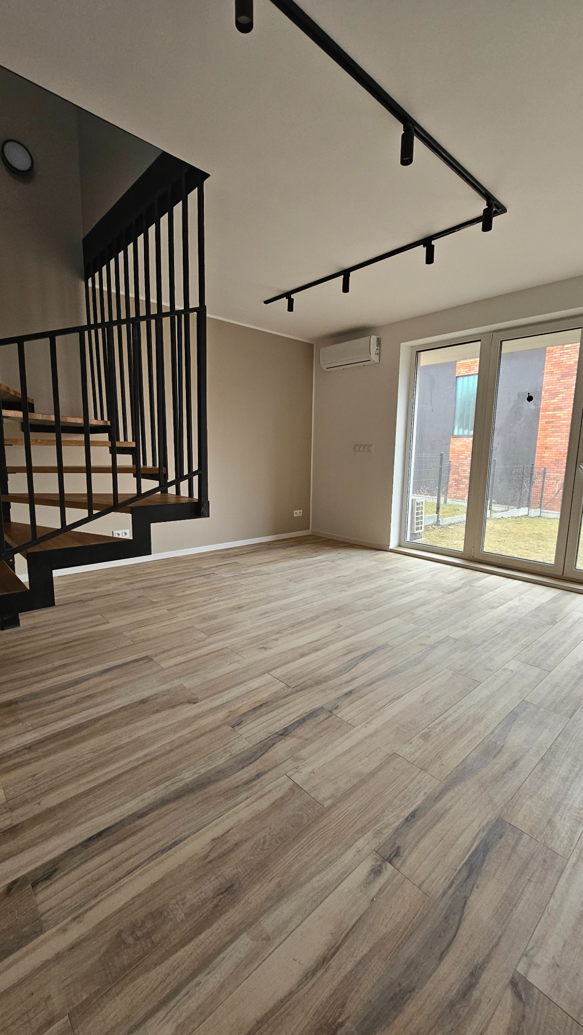 Jasne panele podłogowe z wzorem drewna w przestronnym pokoju z czarnymi schodami i oświetleniem szynowym.