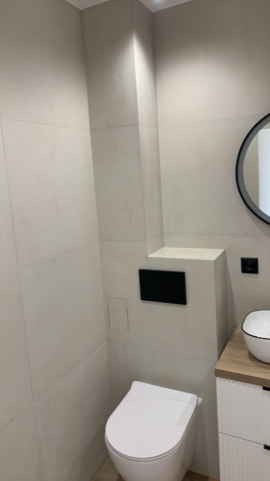 Nowoczesna toaleta w beżowych płytkach, z podwieszanym sedesem i umywalką nablatową z okrągłym lustrem.