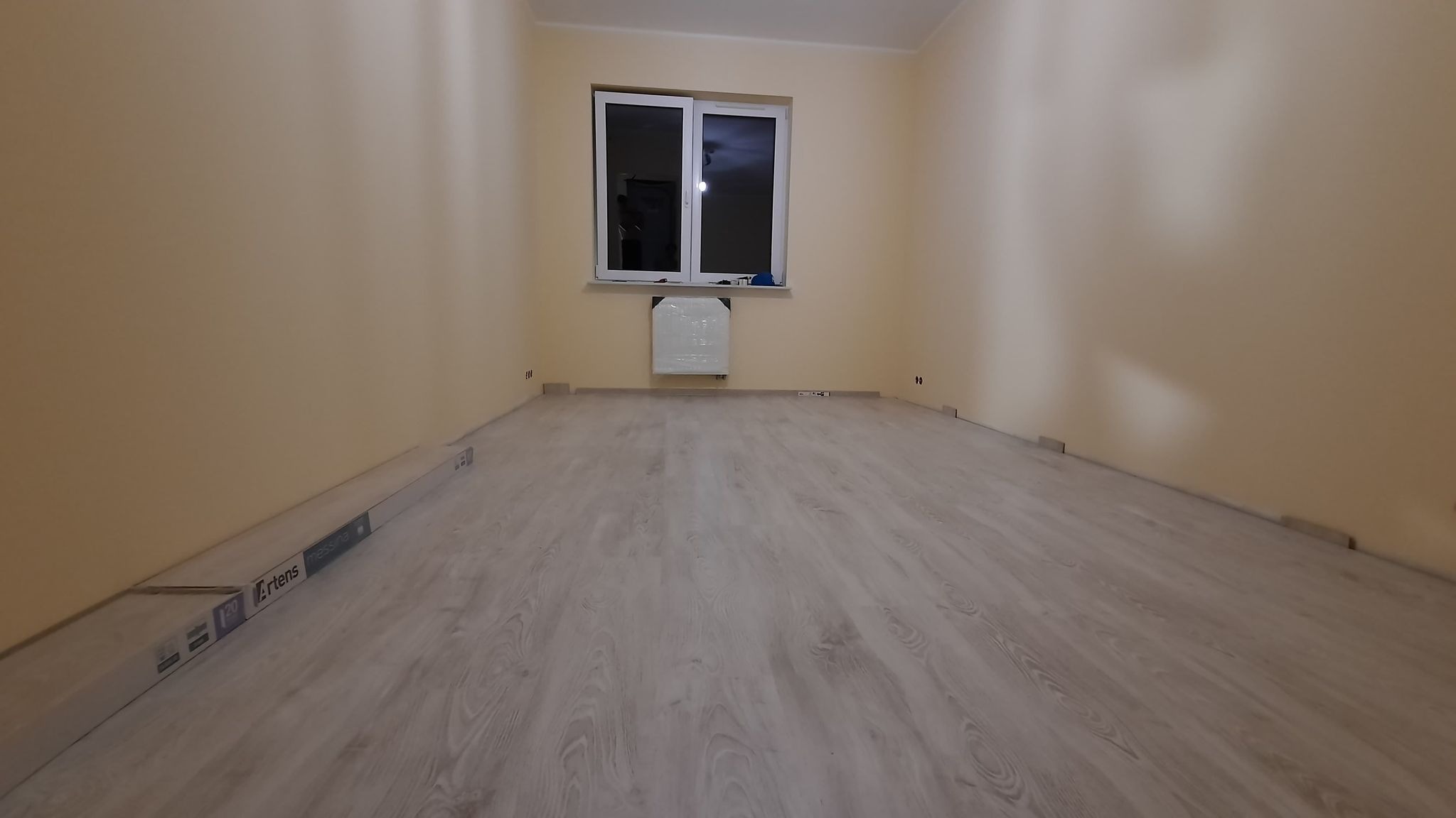 Pokój po ułożeniu paneli podłogowych, widoczne listwy przypodłogowe i opakowanie paneli Artens Messina przy ścianie.