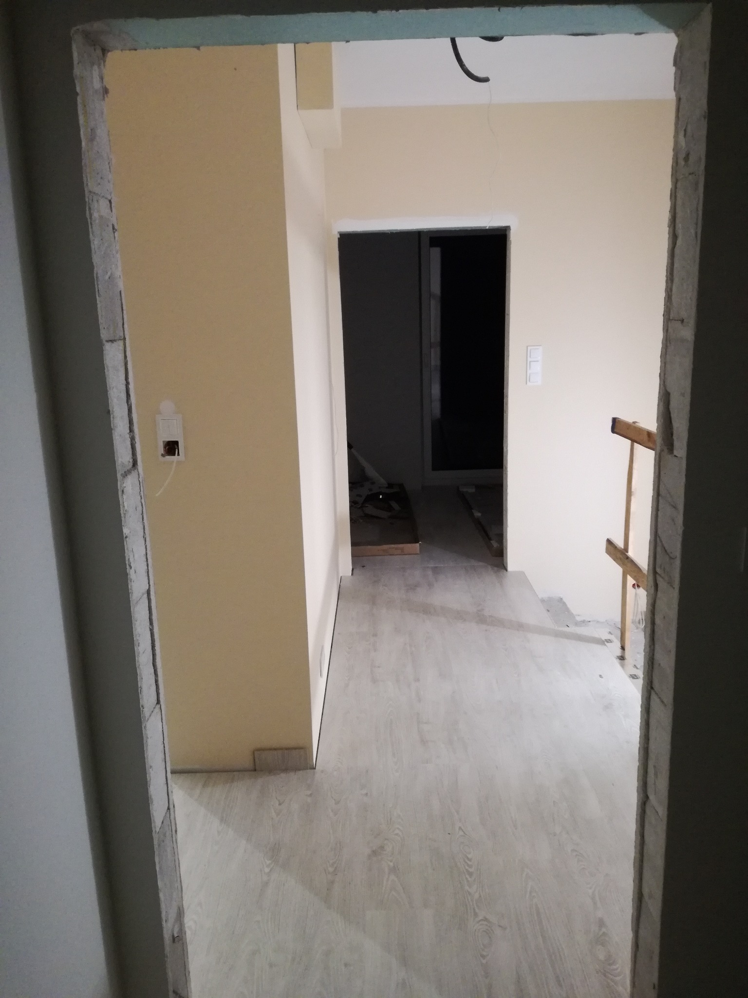 Widok na wnętrze z nową, jasną podłogą z paneli, świeżo pomalowane ściany w odcieniach beżu, widoczne ślady po remoncie na framugach drzwi.